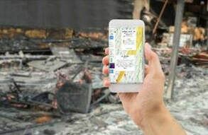 Hand holding a smartphone running LR-x in front of a fire-damaged building